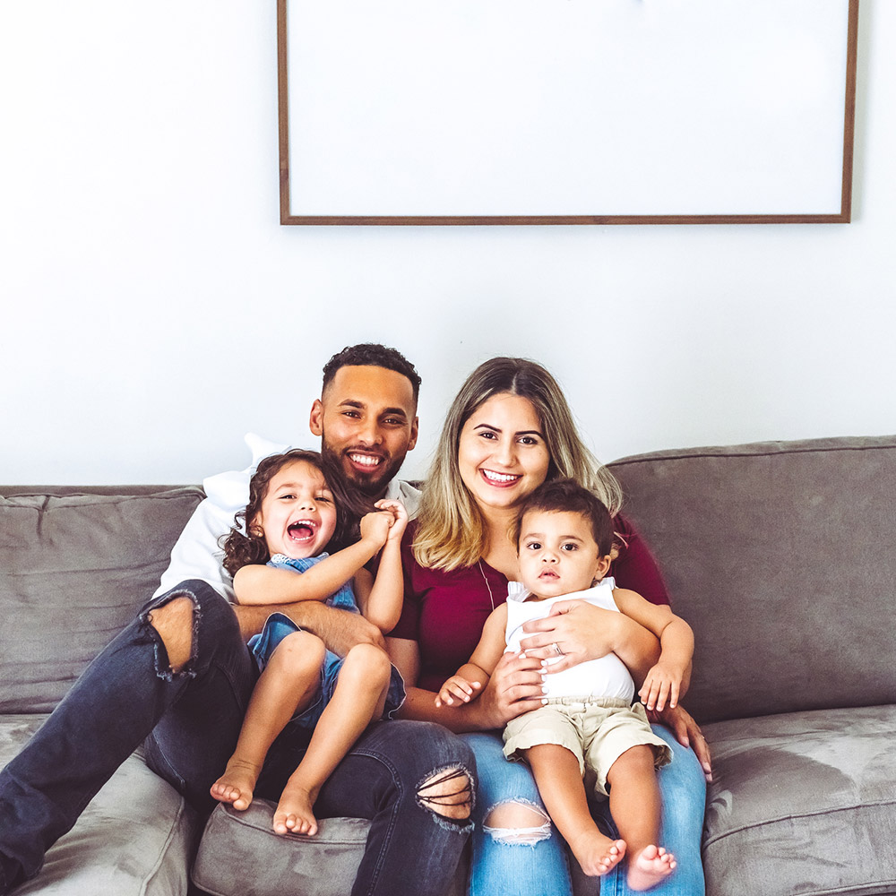 Happy multiracial family at home with two young children in casual portrait on their couch