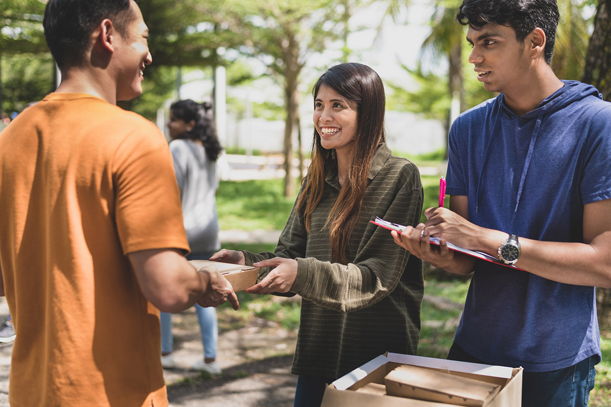 A group of helpful volunteers arranging and packing cardboard boxes with free meals and give away to any needy families and local community facing financial difficulty during an outdoor charity food drive.